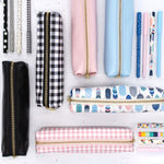 Collection of slim pencil cases, black, buffalo check, ballerina pink check, ballerina pink, feathers and, sky blue.